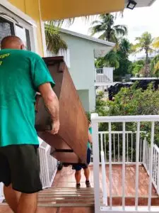Two workers carefully moving furniture on exterior steps