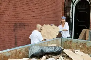 Workers placing debris into a metal dumpster for responsible disposal